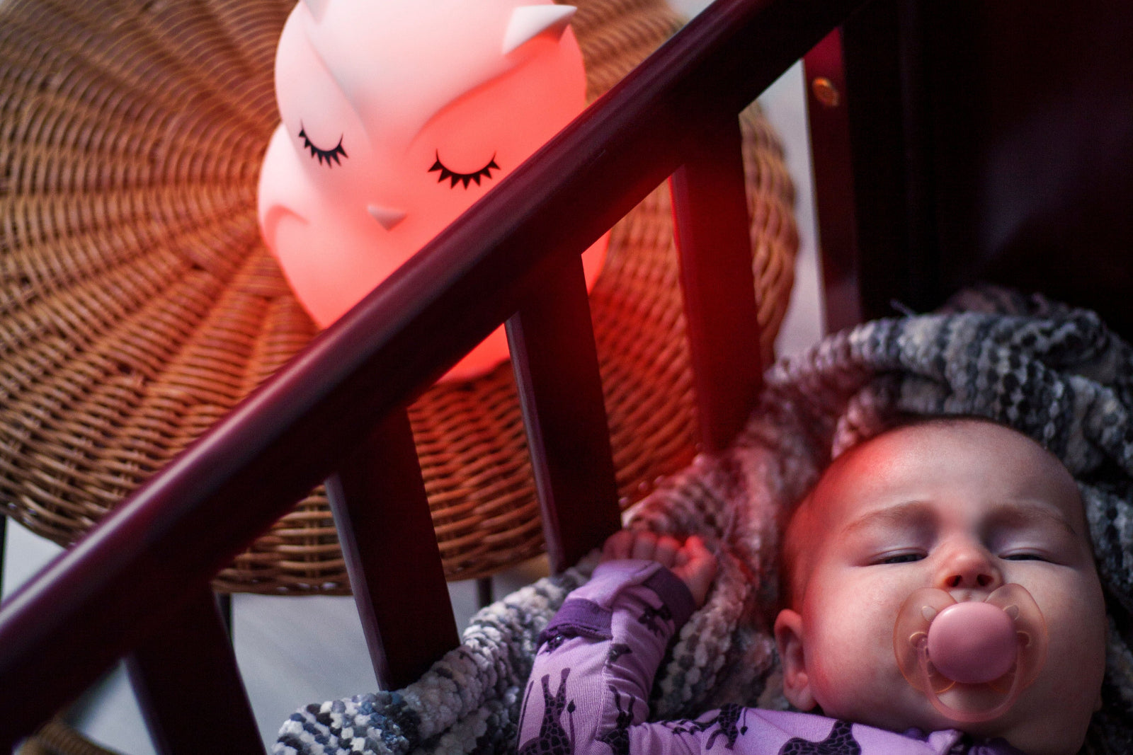 A baby sleeping peacefully in a crib beside their glowing LumiPet owl night light
